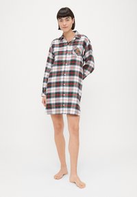 Abito camicia a quadri in bianco, rosso, verde e blu. Chiusura frontale con bottoni, colletto e taschino sul petto con una toppa decorativa. Tessuto morbido.