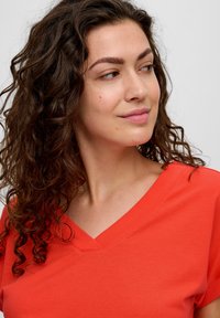 V-hals, korte mouwen top van feloranje stof, met een soepele textuur en een relaxed fit, die de halslijn en schouderdetails accentueert.