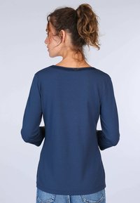 Dunkelblaues Langarmshirt mit Rundhals und weicher Textur, kombiniert mit hellblauen Jeans. Die Rückansicht zeigt eine lockere Passform.