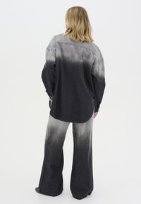 Conjunto de denim negro y gris con efecto ombre. La parte superior presenta un ajuste relajado con botones, mientras que los pantalones son de pierna ancha y con textura.