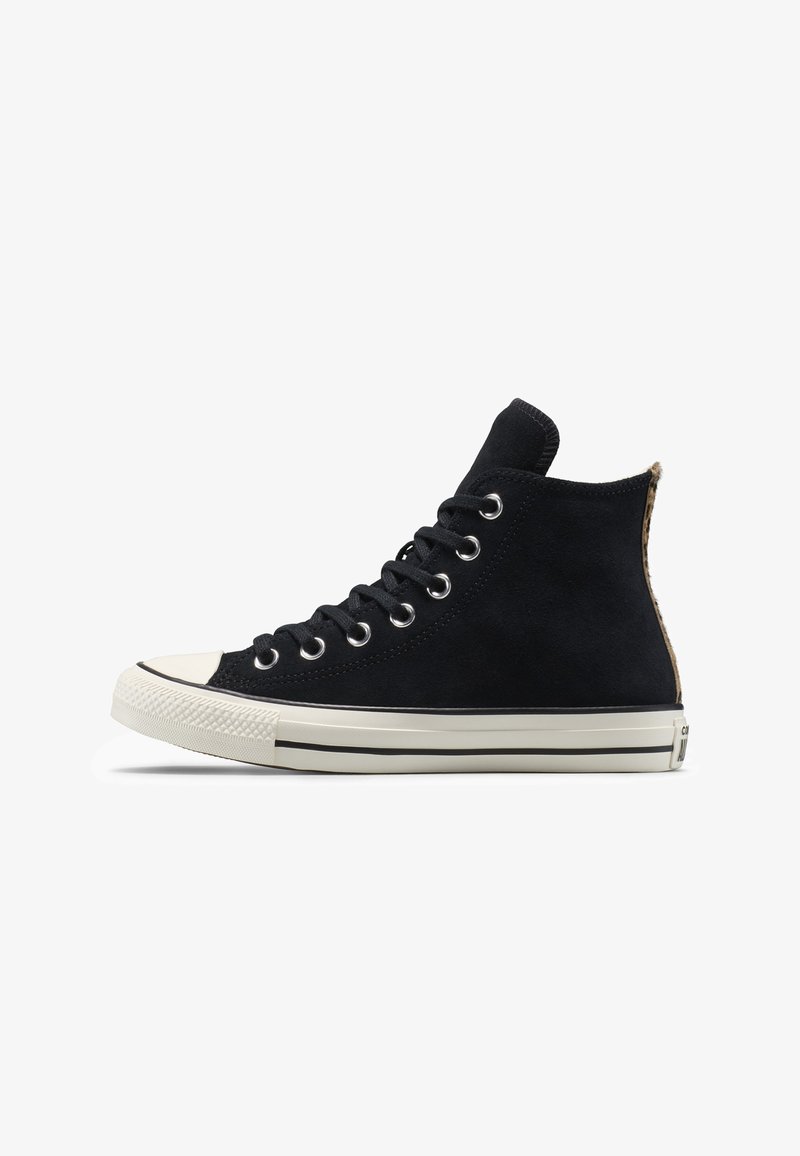 Čierna teniska z semišu s vysokým golierom, bielou gumovou špičkou, kovovými očkami a čiernymi pruhmi na medzipodrážke. Viditeľný textúrovaný detail na zadnej strane.