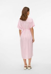 Robe longue, légère et rose avec des manches courtes et une ceinture à nouer à la taille ; le panneau arrière transparent offre un contraste texturé subtil.