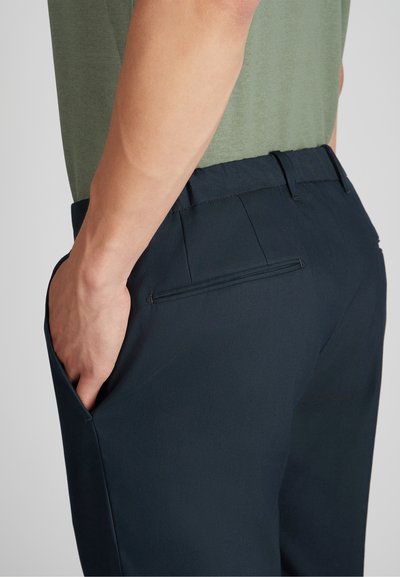 Granatowe spodnie o gładkiej fakturze, z bocznymi kieszeniami oraz jedną tylną kieszenią o wąskim otworze. Dopasowany krój bez widocznych detali szycia.