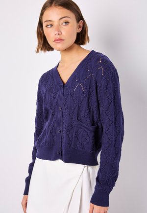 Marineblauer Strickcardigan mit Spitzenmuster, V-Ausschnitt, Knöpfen vorne und einer aufgesetzten Tasche auf der linken Seite.