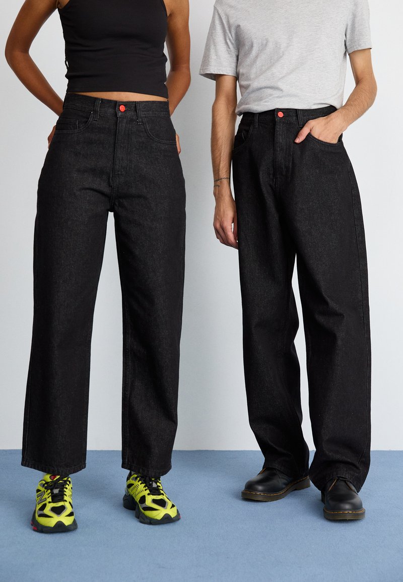 Sorte denim vide bukser med høj talje, med røde knap detaljer. Båret med kontrasterende fodtøj: lysende grønne sneakers og sorte sko.
