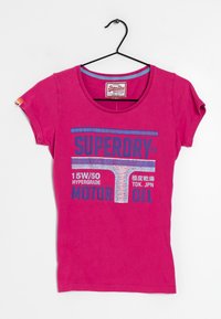T-shirt fuchsia à manches courtes en coton, présentant un motif graphique bleu avec le texte "SUPERDRY" et "MOTOR OIL". Encolure ronde.