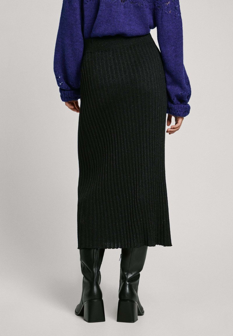 Falda midi negra con plisados que presenta una cinturilla ajustada, tejido texturizado y un sutil brillo, combinada con elegantes botas negras hasta la rodilla.