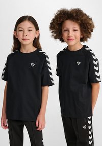 T-shirt in cotone nero a maniche corte, con motivi a zig-zag bianchi sulle spalle e un piccolo logo sul petto. Vestibilità casual.