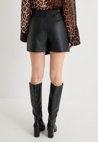 Zwarte leren shorts met een gladde textuur, hoge taille en achternaaddetail, gecombineerd met kniehoge zwarte haklaarzen.