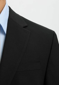 Zwarte blazer met een textuurafwerking, enkele notched revers en een borstzak. Draagt over een lichtblauw gestreept shirt.
