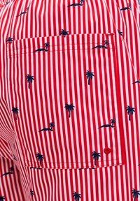 Κόκκινο και άσπρο υφασμάτινο ύφασμα με κάθετες ρίγες και σχέδια σε σκούρο μπλε με φοίνικες και νησιά, με ραμμένη ορθογώνια τσέπη.