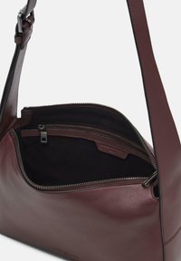 Ciemnobordowa skórzana torba na ramię z regulowanym paskiem, otwierana u góry na zamek, odsłaniająca czarne wnętrze z tkaniny z kieszenią na zamek.