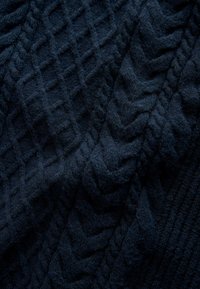 Dunkelblauer, strukturierter Strickstoff mit einer Mischung aus erhabenen Rautenmuster und Zopfmustern, die ein weiches und dickes Erscheinungsbild erzeugen.