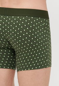 Zöld boxeralsó világoszöld és fehér virágmintával. Tömör zöld derékpánttal és szűkített fazonnal rendelkezik.
