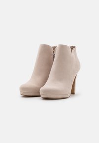 Beige Wildleder-Stiefeletten mit runder Zehenpartie, seitlichem Reißverschluss und hohem Blockabsatz. Glatte Textur mit minimalistischem Design.