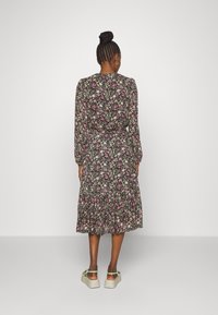 Mustapohjainen kukallinen midi-mekko, jossa vaaleanpunaisia ja valkoisia kukkia. Pitkät hihat, vyötärö istuu, ja kerroksittainen hame. Mallilla on vaaleanvihreät sandaalit.