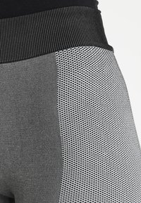 Los leggings negros y grises presentan un patrón texturizado con una cinturilla ancha y elástica. El material es elástico, lo que mejora la comodidad y el ajuste.