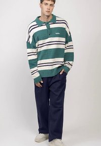 Randig tröja i teal, vitt och marinblått, med krage och tre knappar. Kombinerad med vida marinblå byxor och vita sneakers.