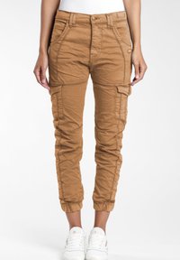 Pantalones cargo marrones con puños elásticos, que presentan múltiples bolsillos, un tejido texturizado y un diseño ajustado. Combinados con zapatillas blancas.