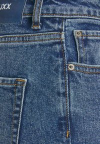 Denim-Jeans in einem ausgewaschenen Blauton mit auffälligen Nähten in einem kontrastierenden Orangeton, einer Fronttasche und einem Metallschließknopf.