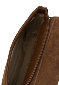 Interno di una borsa in pelle scamosciata e pelle marrone che mostra una morbida fodera in tessuto e una tasca con cerniera lungo un lato.