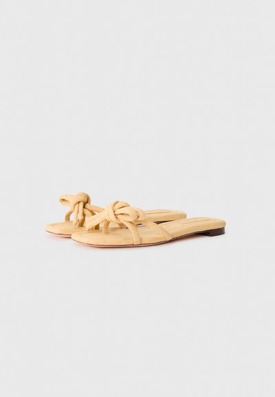 Sandales plates en tissu jaune avec des sangles nouées et une surface texturée, dotées d'une semelle marron basse pour le confort et la facilité de port.