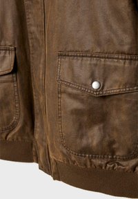 Giacca in pelle marrone con due tasche frontali, orlo a coste e una texture liscia con sottili variazioni di colore. Chiusure a scatto argento.