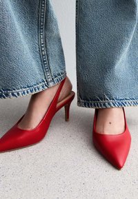 Röda läder slingbacks med spetsig tå, med en smal, gyllene klack, och bärs med ljusblå vida jeans.