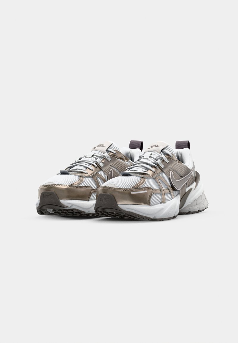 Zapatillas Nike con un diseño de materiales mixtos que incluyen malla gris, acentos plateados y una suela blanca. Presentan detalles reflectantes y cordones resistentes.