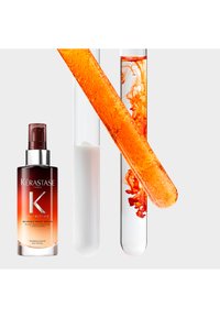 Serum Kérastase Nutritive 8H Magic Night w ciemnej bursztynowej butelce, obok przezroczystych fiolek z pomarańczowym płynem wirującym w środku.