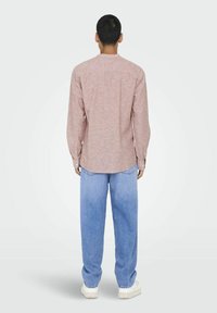Camicia a maniche lunghe a righe rosse e bianche con orlo curvo, indossata con jeans azzurri larghi e sneakers bianche.