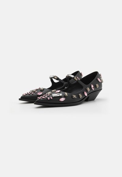 Black leather shoes with a pointed toe and low wedge heel, adorned with various pink and silver embellishments.
