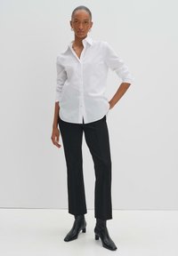 Camicia bianca in cotone con maniche arrotolate, abbinata a pantaloni neri attillati e stivaletti neri. Design semplice e classico.