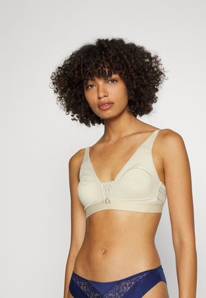 Beige wireless bra with a textured, mesh design, deep V-neck, and a front clip closure. Features wide straps for support.