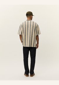 Short-sleeve, beige and navy striped shirt with a relaxed fit; paired with dark pants and brown shoes. Back view, minimalistic design.