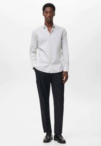 Camisa blanca a rayas con botones y mangas largas, combinada con pantalones oscuros ajustados y zapatos negros. Textura suave y diseño ajustado.
