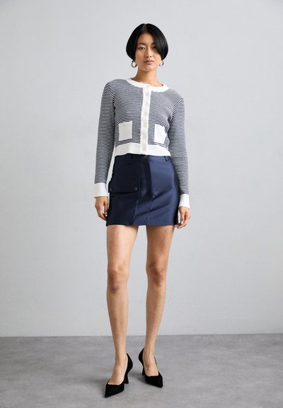 Stripete cardigan i marineblå og hvit med to frontlommer, kombinert med et tettsittende marineblå miniskjørt med en sidelomme og knappelukking.