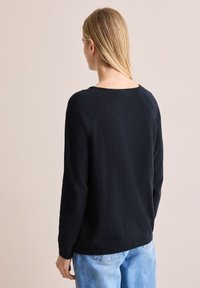 Schwarzer Pullover mit langen Ärmeln, rundem Halsausschnitt und gerippten Bündchen, mit glatter Textur und lockerer Passform, kombiniert mit hellblauen Jeans.