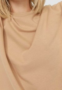 Pull en maille beige avec un col côtelé et une texture douce, tombant doucement autour du corps avec une coupe décontractée.