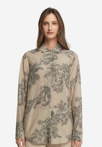 Beige långärmad blus i mjukt tyg, med invecklade blommiga och paisleymönster i mörkblått och silver. Knappställd design.