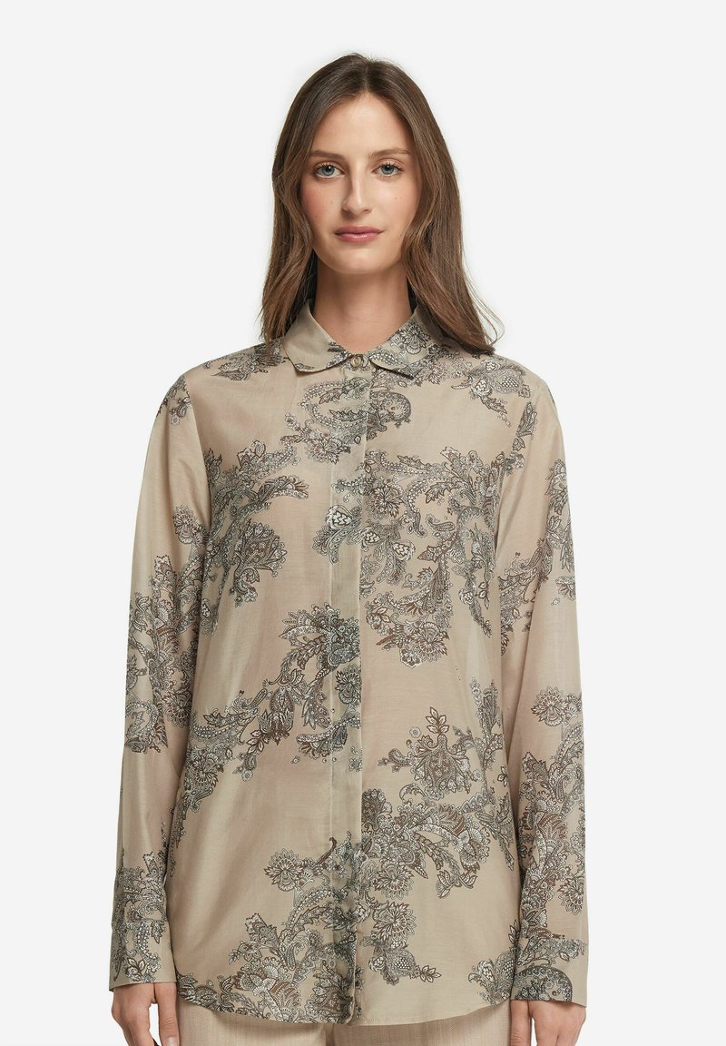 Beige långärmad blus i mjukt tyg, med invecklade blommiga och paisleymönster i mörkblått och silver. Knappställd design.