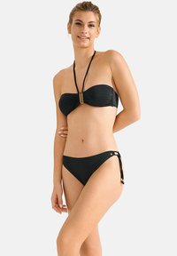 Zwarte bikini met een bandeau-top met een centrale gouden accent en dunne bandjes. De onderkant heeft zijknopen en een afgerond ontwerp. Glad textuur.