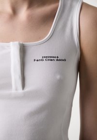 Bílý bezrukávový top s kulatým výstřihem, předním zapínáním na knoflíky a černým potiskem značky "CONVERSE Feng Chen Wang."