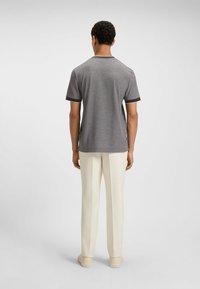 Gray short-sleeve shirt featuring contrasting black trim at sleeves and collar, paired with light-colored trousers and beige shoes.