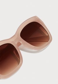 Ochelari de soare supradimensionați cu un cadru din plastic roz translucid și lentile gradient de culoare maro, având o textură netedă și lucioasă.