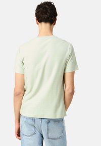 Ljusgrön kortärmad T-shirt i mjuk bomull med rund halsringning och avslappnad passform, som bärs med ljusblå jeans.