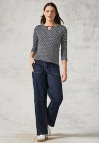 Långärmad topp med diamantmönster i grått och vitt, kompletterad med mörka jeanstights och vita sneakers med svarta detaljer.