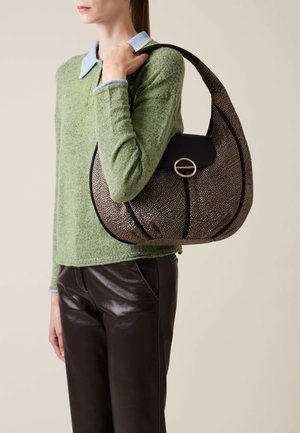 Black and gold patterned hobo bag with a rounded shape, textured fabric, and a gold circular hardware accent, worn on a green sweater.