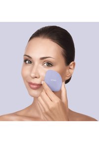 Lilla ansigt værktøj holdt mod kind, let buet design med glat tekstur, mærket "GESKE." Modellen har klar hud og naturlig makeup.
