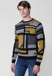 Suéter con un patrón geométrico en negro, gris y mostaza. Confeccionado en tejido de punto, presenta un cuello redondo y puños acanalados.